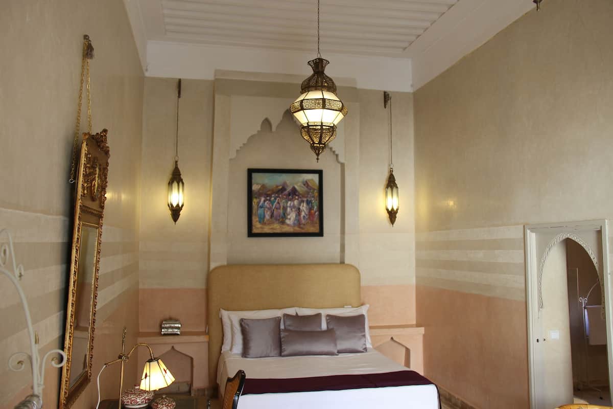 A hotel room with a bed, a large mirror, a painting on the wall, and two wall-mounted lamps.