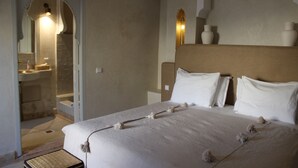 Habitación de hotel con cama, mesita de noche, espejo y baño visible a través de una puerta abierta.