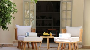 Dos sillas de madera con cojines blancos y una pequeña mesa con frutas y una bebida.