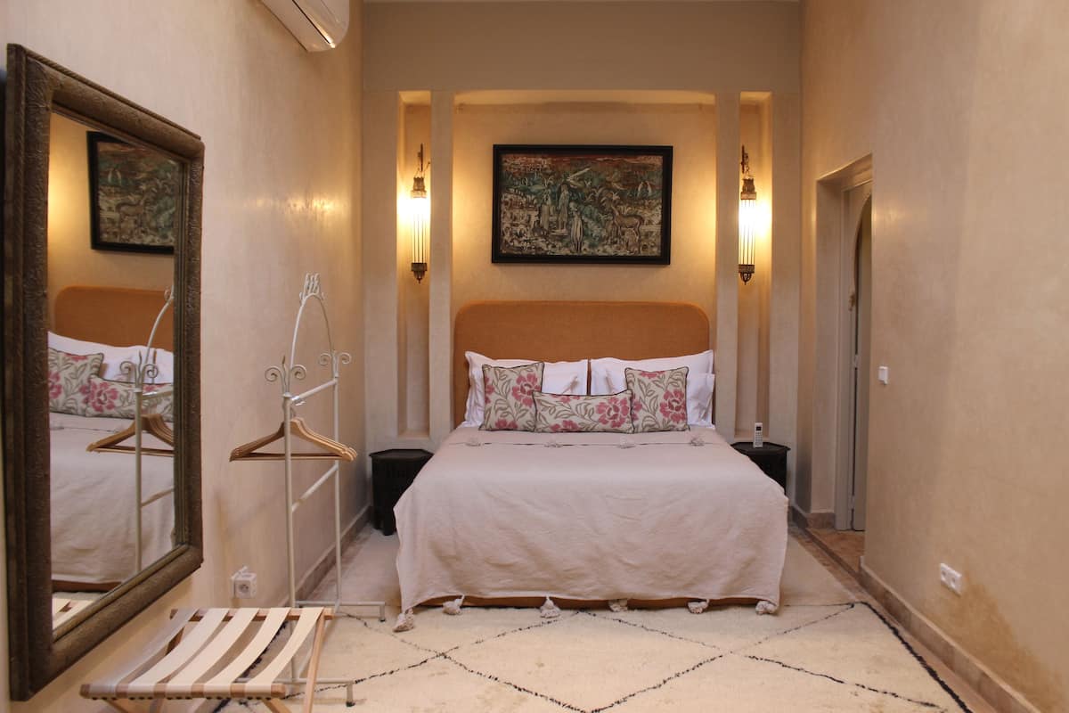 A hotel room with a large bed, a mirror, a wardrobe, and a painting on the wall.