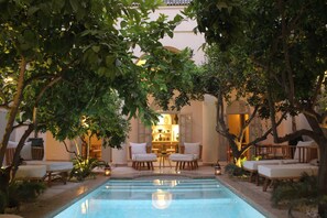 An indoor swimming pool with lounge chairs and a seating area, surrounded by trees and plants. - Riad Emberiza Sahari (Marrakech)