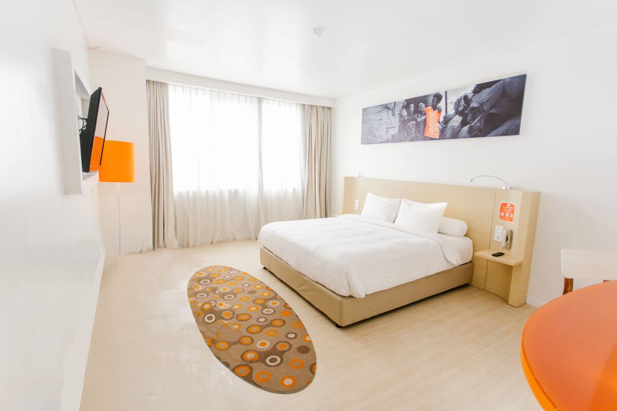 Une chambre d’hôtel avec un lit, une table de chevet, une lampe, un tableau au mur et une fenêtre avec des rideaux.