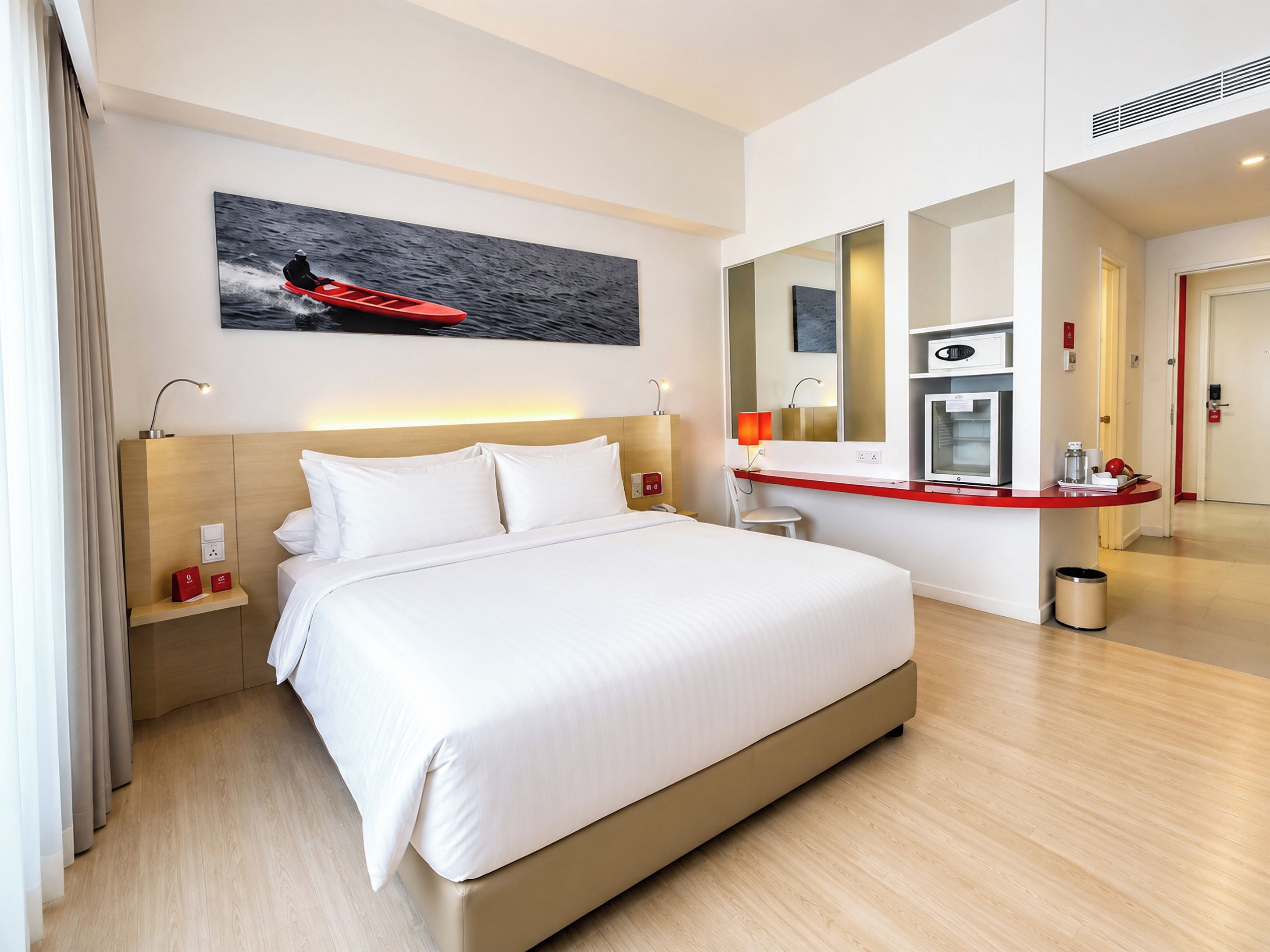 A hotel room with a large bed, a desk with a computer, a mirror, and a painting of a kayak on the wall.