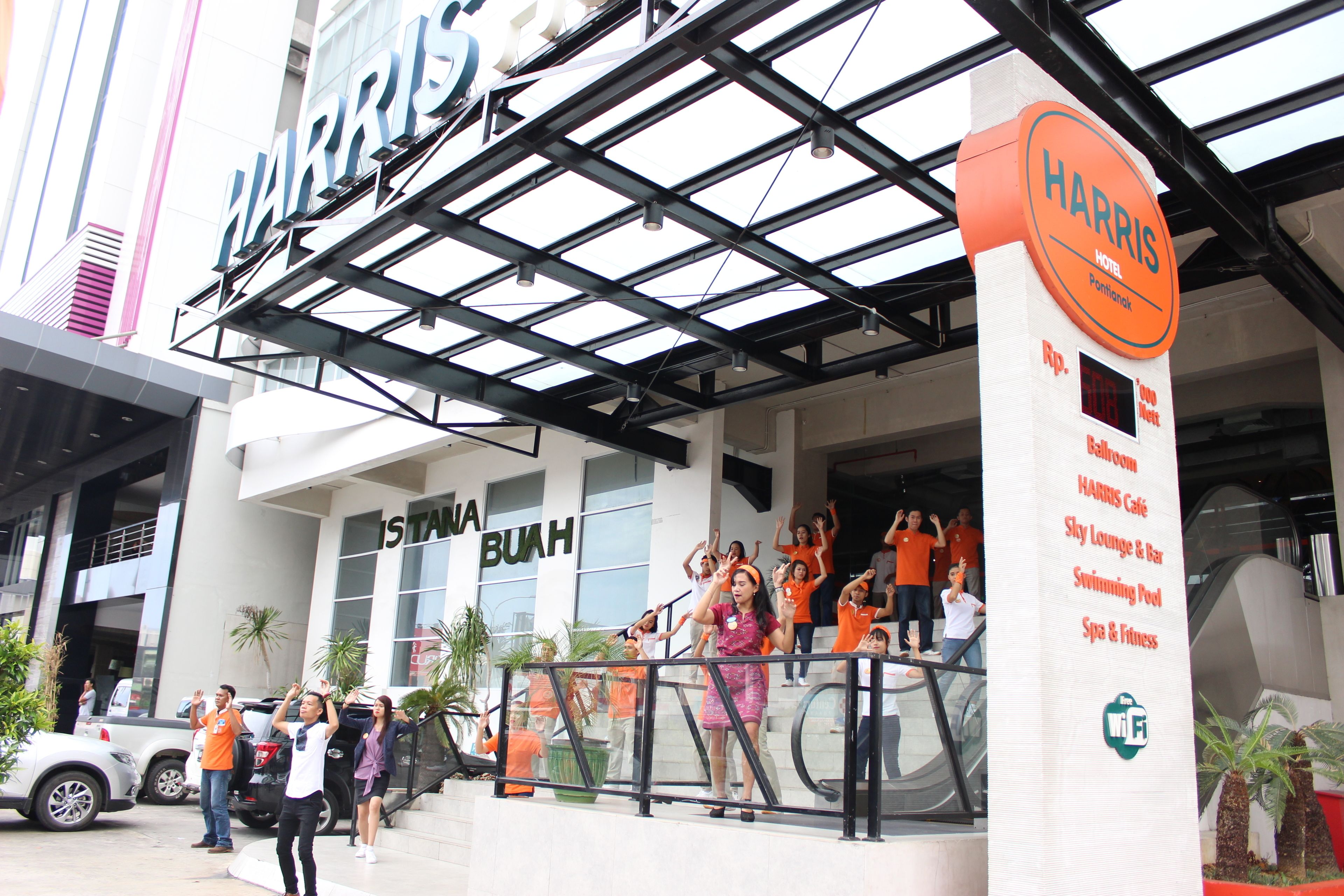A Harris Hotel with a modern glass facade, a visible staircase, and a sign listing amenities like a swimming pool and fitness center.