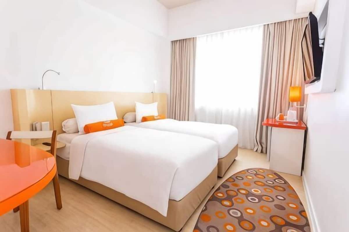 Une chambre d’hôtel avec un lit, un bureau, une chaise, une télévision et une fenêtre avec des rideaux.