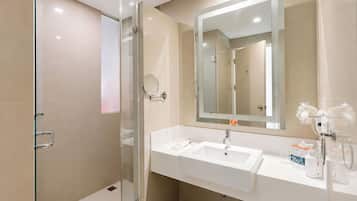 Un baño moderno con cabina de ducha de vidrio, un espejo grande y un lavamanos blanco con artículos de aseo.