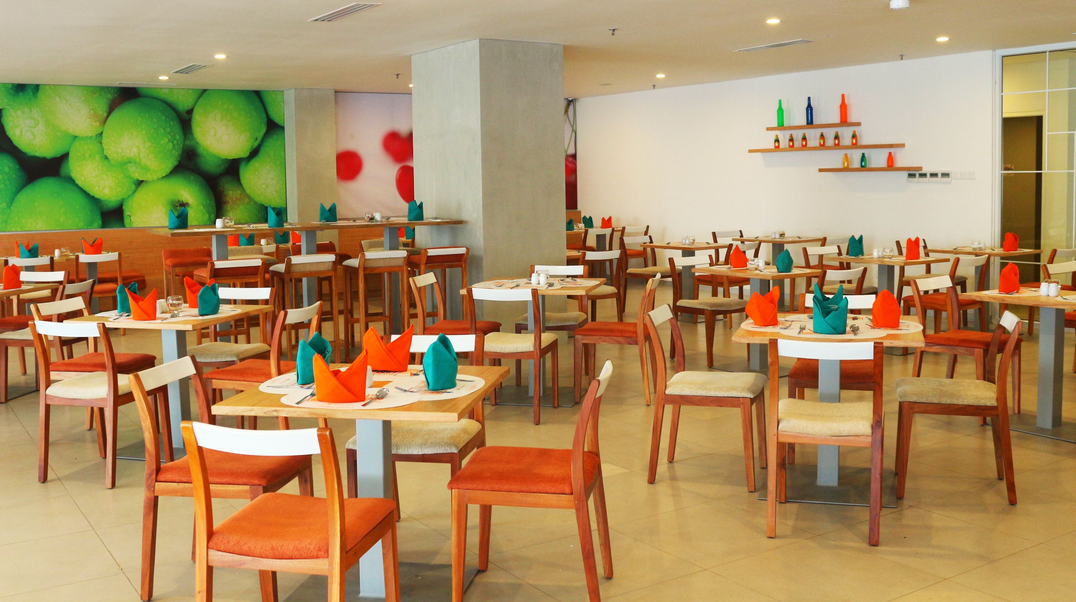 A spacious dining area with multiple tables and chairs, each set with orange napkins and cutlery.