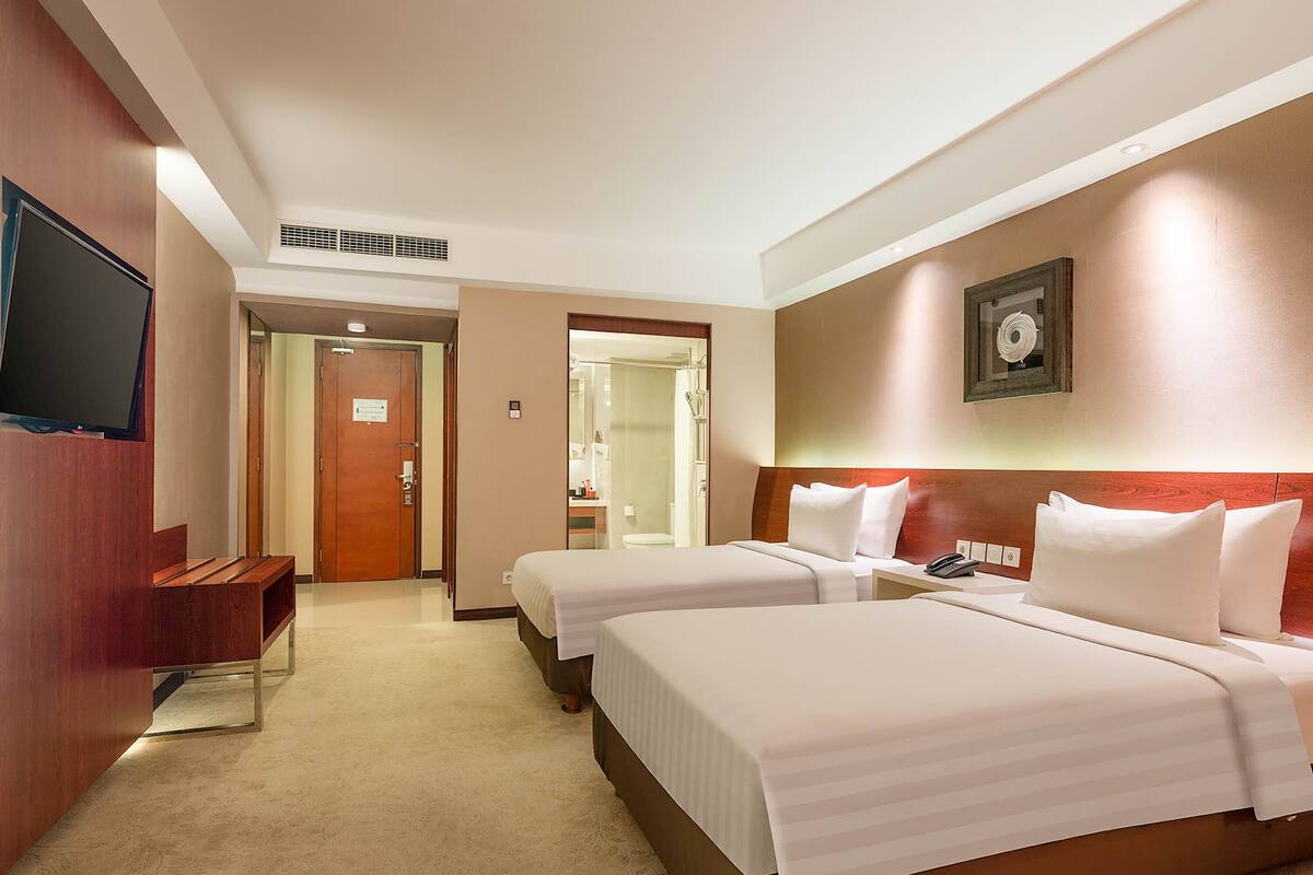 A hotel room with two beds, a TV, a desk, and a bathroom visible through an open door.