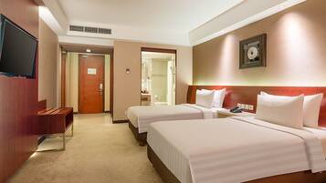 A hotel room with two beds, a TV, a desk, and a bathroom visible through an open door.