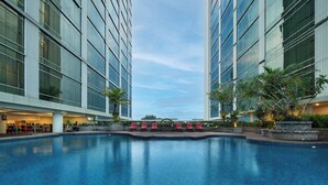 Um hotel moderno com piscina central, espreguiçadeiras e um jardim bem cuidado.