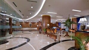 Um hall amplo com piso de mármore, balcão de recepção, área de estar e plantas decorativas.