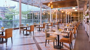 Um restaurante amplo com pé direito alto, grandes janelas e luminárias modernas.