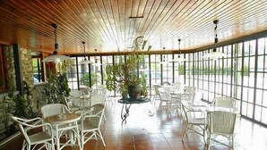 A spacious indoor area with a high ceiling, large windows, and several tables and chairs. - Hotel San Ángel (Ribadedeva)