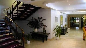A spacious interior with a curved staircase, a large potted plant, and a hallway leading to another room. - Hotel San Ángel (Ribadedeva)