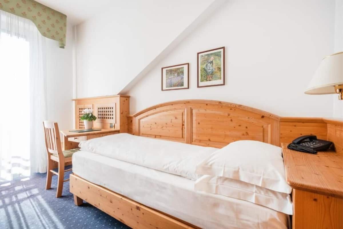 A wooden bed with a headboard, a desk with a chair, a lamp, and two framed pictures on the wall.