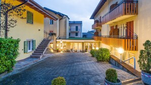 A courtyard with a paved walkway, a staircase leading to a second floor, and a building with a balcony. - Hotel Lucia (Levico Terme)