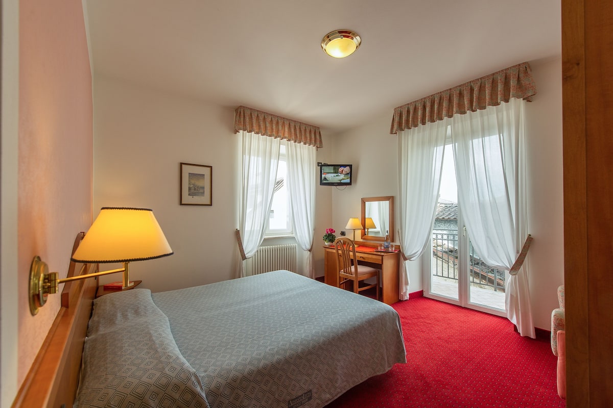 A hotel room with a bed, a desk with a chair, a television, and a window with curtains.