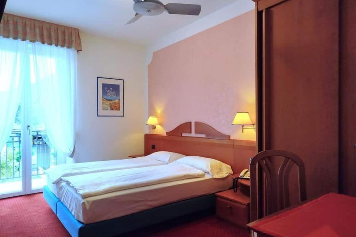 A hotel room with a bed, bedside lamps, a desk, a chair, and a ceiling fan.