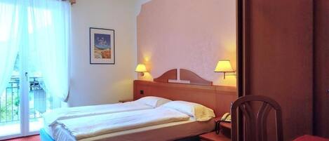 Una habitación de hotel con cama, lámparas de noche, escritorio, silla y ventilador de techo.