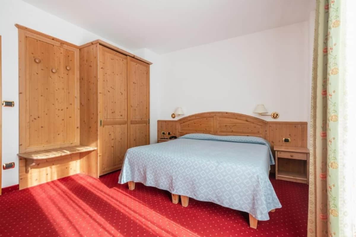 A bedroom with a bed, wooden wardrobe, bedside tables, and a red carpet.