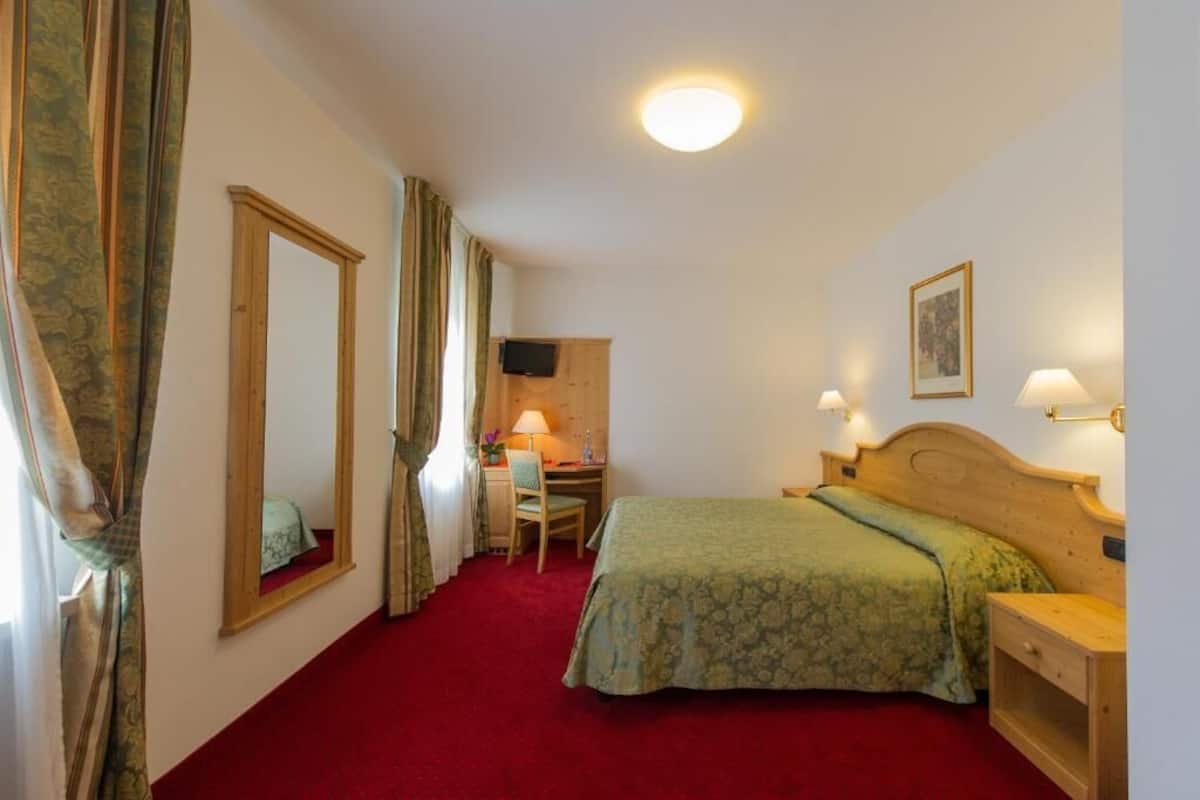 A hotel room with a bed, desk, chair, and a television on the wall.