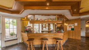 A bar area with wooden bar stools, a variety of bottles on the shelves, and a window with curtains. - Hotel Lucia (Levico Terme)