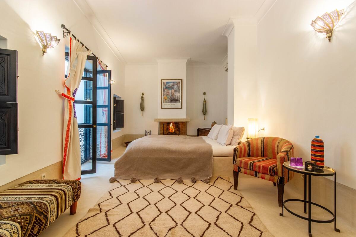 A bedroom with a bed, a sofa, a patterned rug, and a small table with decorative items.