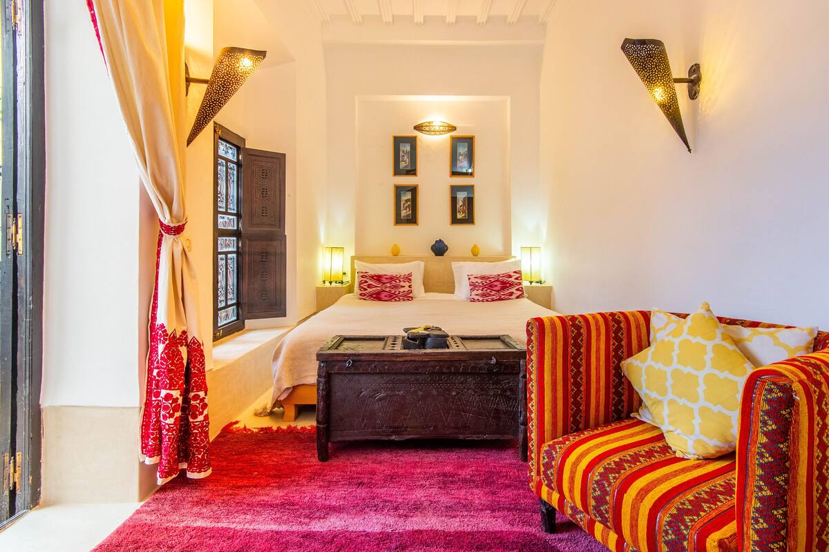 A room with a bed, a wooden chest, a sofa, and a window with curtains.