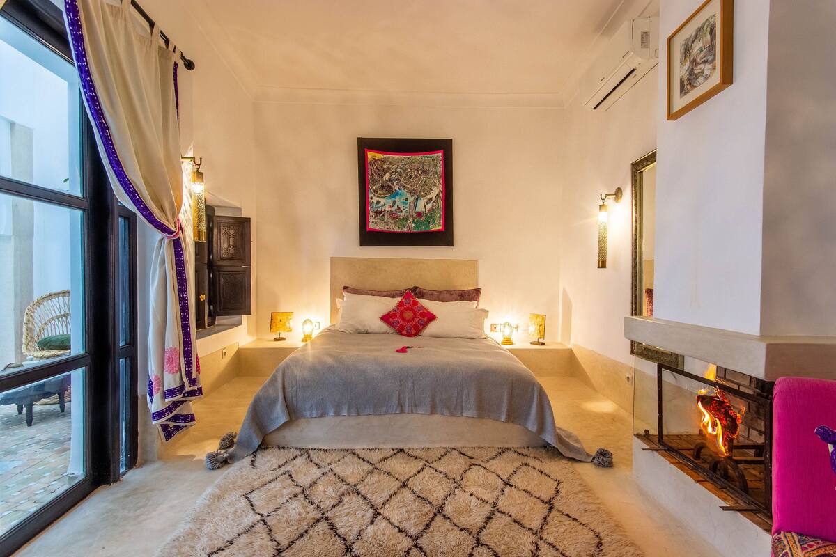 A bedroom with a bed, a fireplace, and a large window.