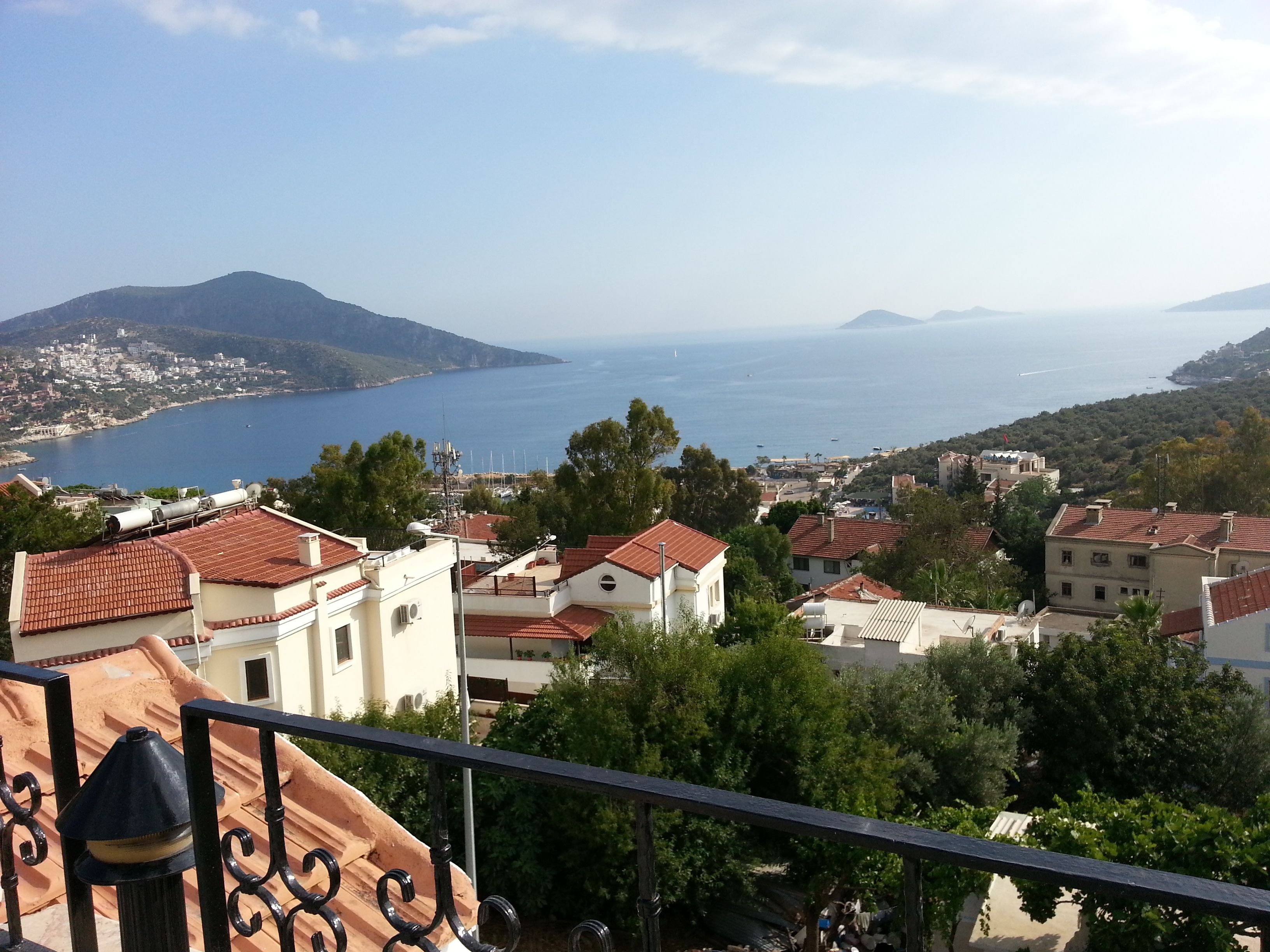 A coastal town with terracotta-roofed buildings, a clear view of the sea, and distant mountains.