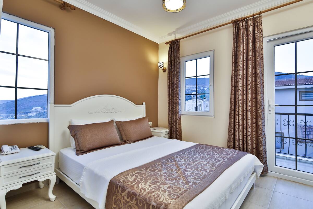 Habitación de hotel con una cama grande, una mesita de noche con teléfono y vistas a la ciudad a través de una ventana.