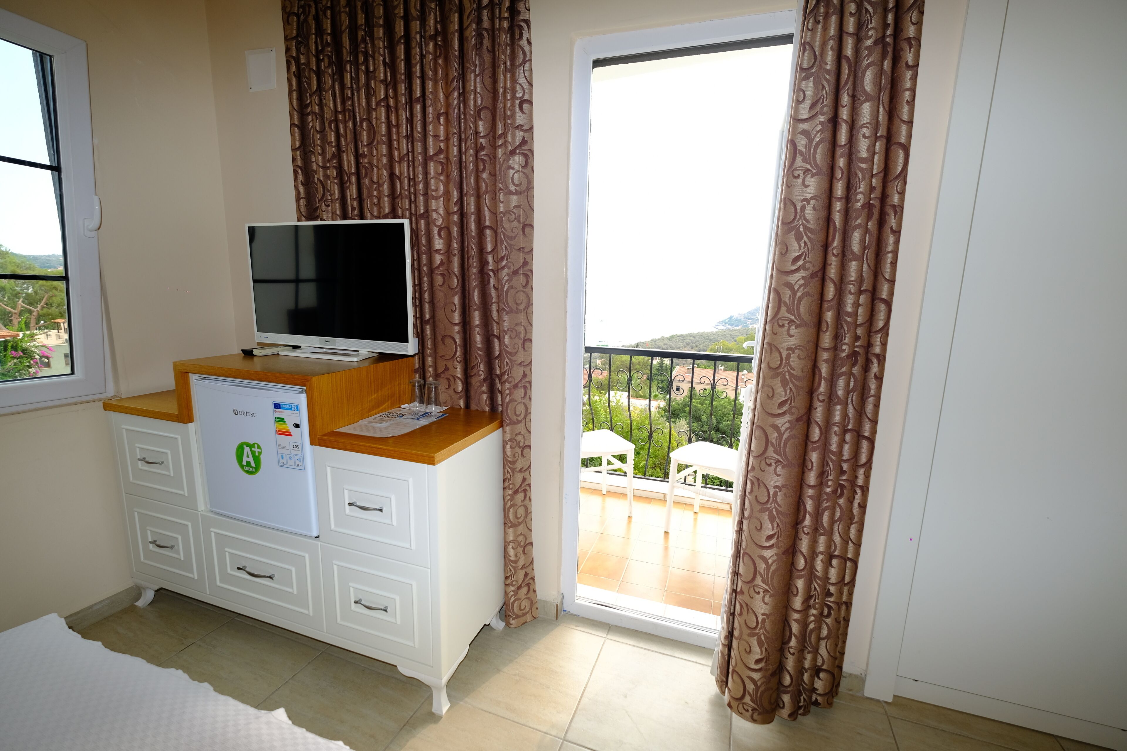 A room with a TV on a wooden cabinet, a mini-fridge, and a balcony with a view.