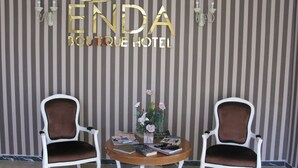 A room with two white upholstered chairs, a small round table with magazines and a vase of flowers, and a striped wall with the text "ENDA BOUTIQUE HOTEL". - Enda Boutique Hotel (Kas)