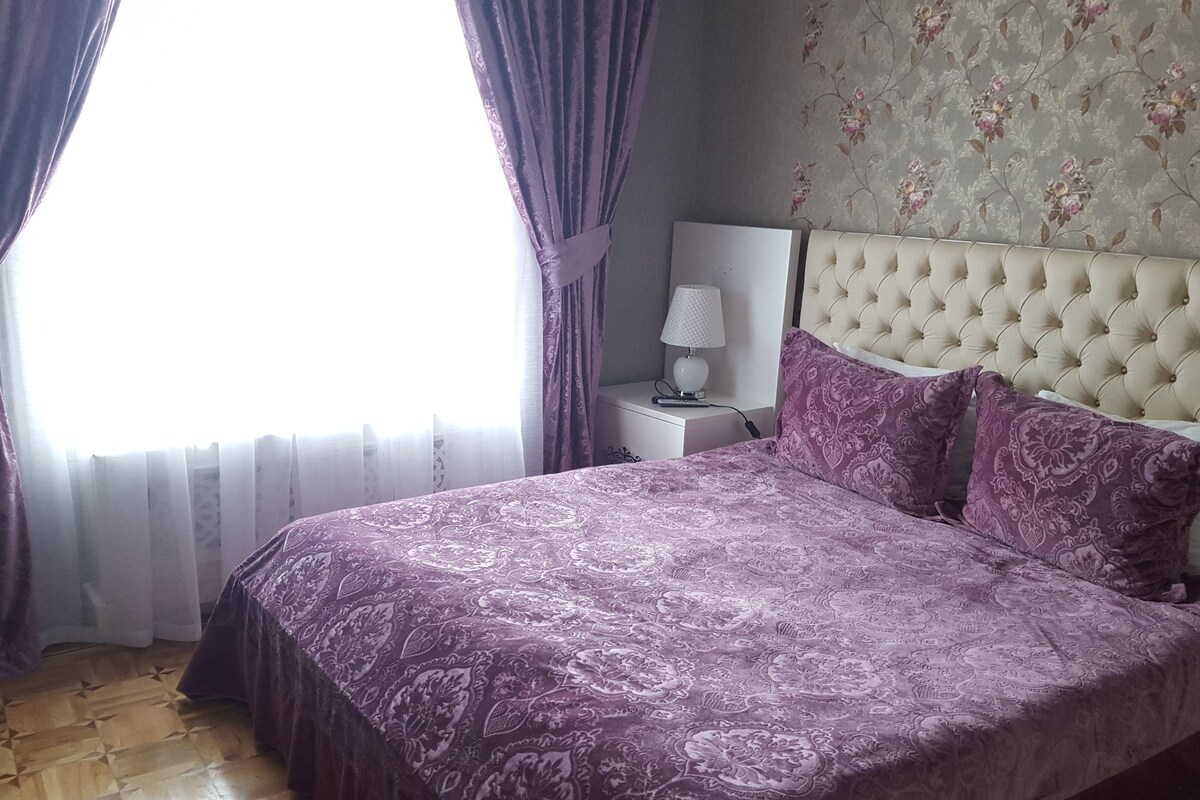 Une chambre à coucher avec un lit, des rideaux, une table de chevet, une lampe et un papier peint à motifs floraux.