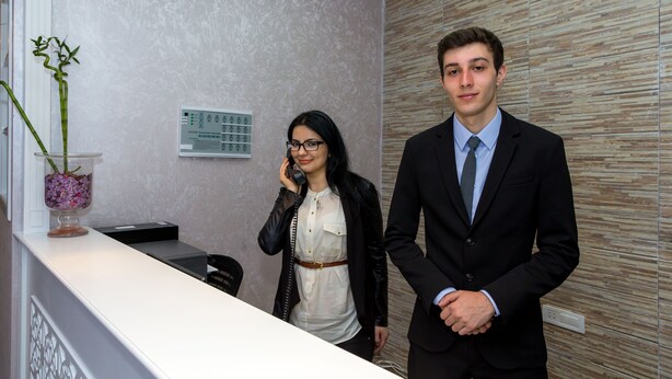 A reception area with a reception desk, a plant, and a wall-mounted control panel. - Premier Old Gates (Baku)