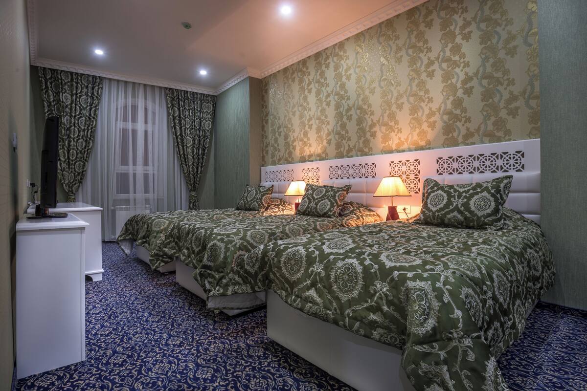 A hotel room with two beds, a desk, a mirror, patterned wallpaper, and a patterned carpet.