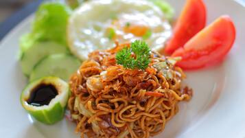 A plate of noodles topped with fried shallots, garnished with parsley, accompanied by a fried egg, slices of cucumber, tomato, and a half avocado.