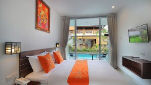A hotel room with a large bed, a telephone on the nightstand, a TV on the wall, and a view of the pool and building outside. - Lotus Tirta Seminyak (Seminyak)