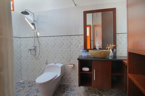 A bathroom with a toilet, shower, and wooden vanity with a large mirror. - Lotus Tirta Seminyak (Seminyak)