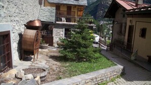 A stone building with a wooden barrel and a small tree in the courtyard. - Hotel Ottoz Meublè (Courmayeur)