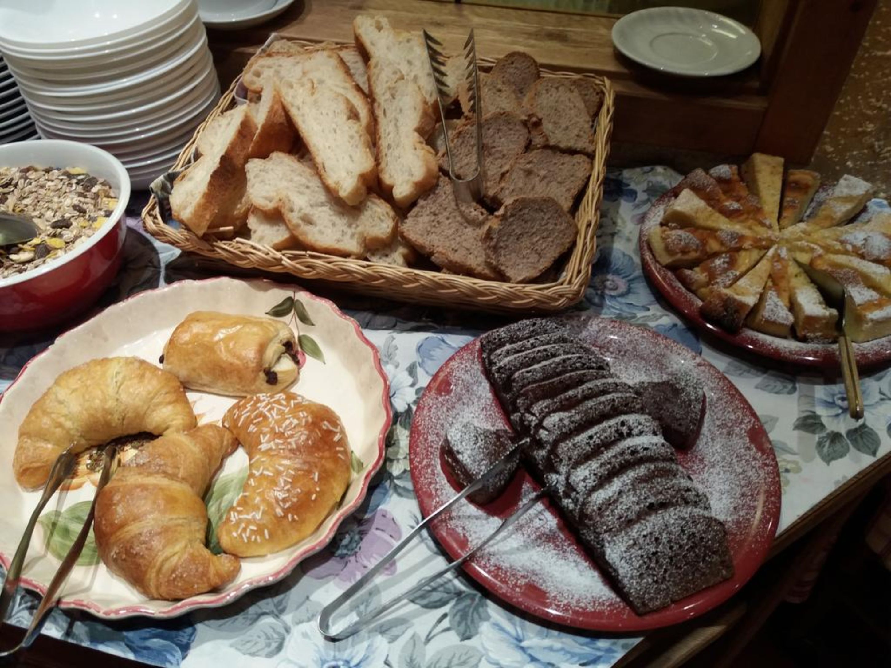 A buffet table with various breads, pastries, and a dessert.