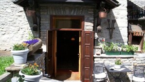 A stone building with a wooden door, outdoor seating, and potted plants. - Hotel Ottoz Meublè (Courmayeur)