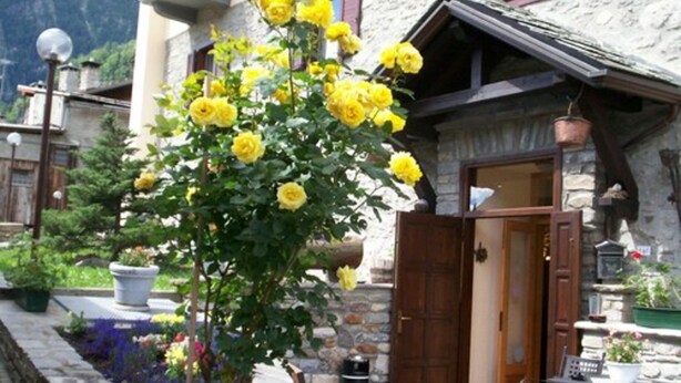 A stone building with a wooden door and a balcony with a table and chairs. - Hotel Ottoz Meublè (Courmayeur)