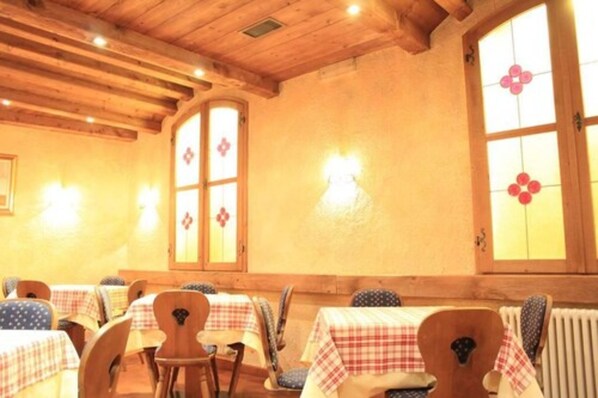 A restaurant with wooden beams, checkered tablecloths, and large windows with floral designs.