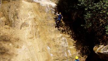 A person rappelling down a rocky cliff into a body of water, with another person standing in the water below.