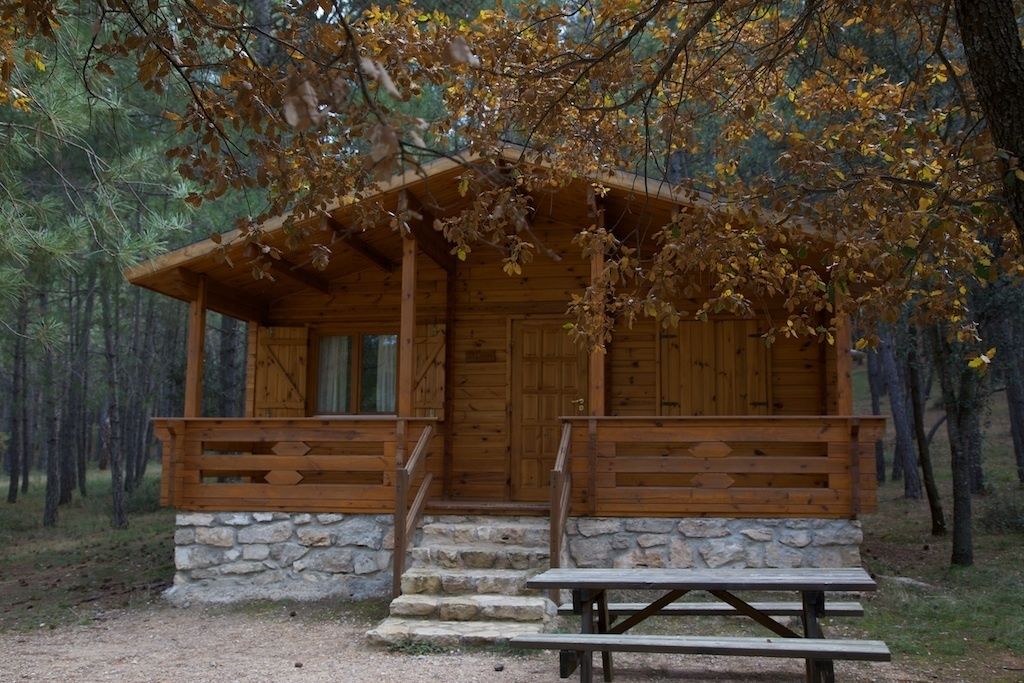 Una cabaña rústica con base de piedra, fachada de madera y un porche con escalones que llevan a una puerta de madera.