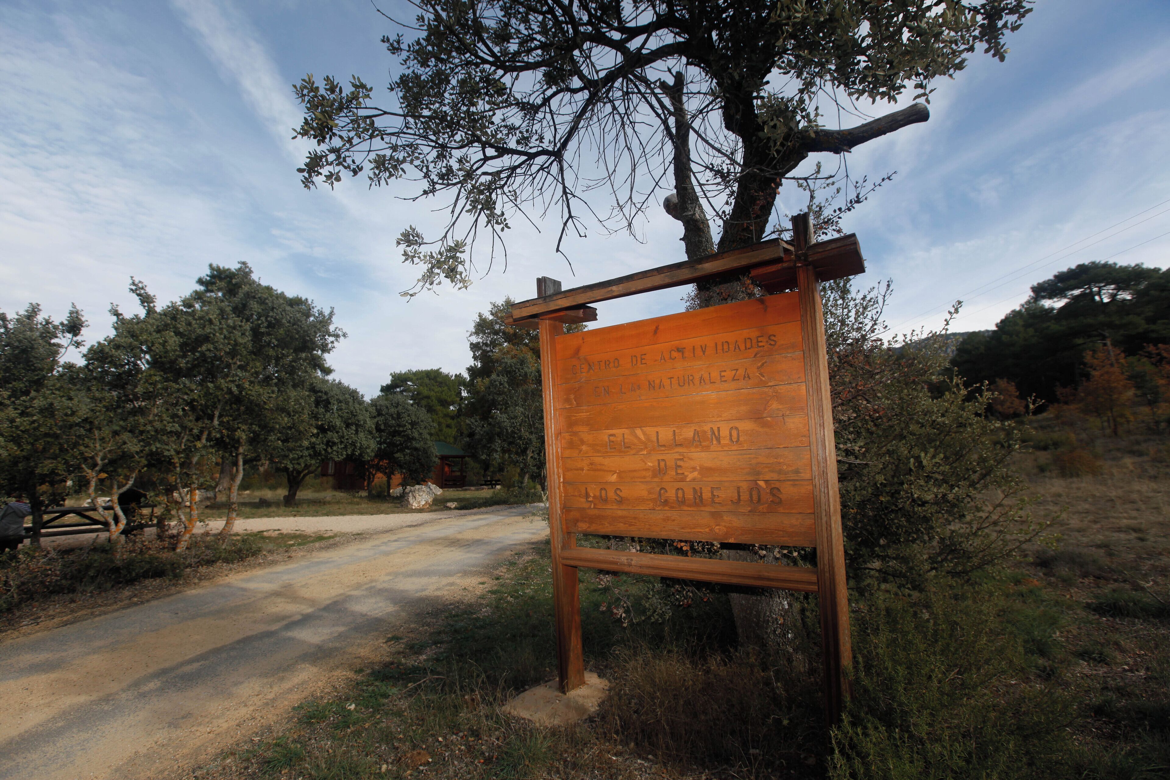 Un cartel de madera con texto en español, situado al lado de un camino de tierra con árboles y cielo despejado al fondo.