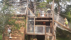 Una casa árbol de madera con un puente de cuerda, rodeada de árboles.
