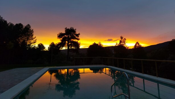 Una piscina con vista a una puesta de sol y árboles al fondo.