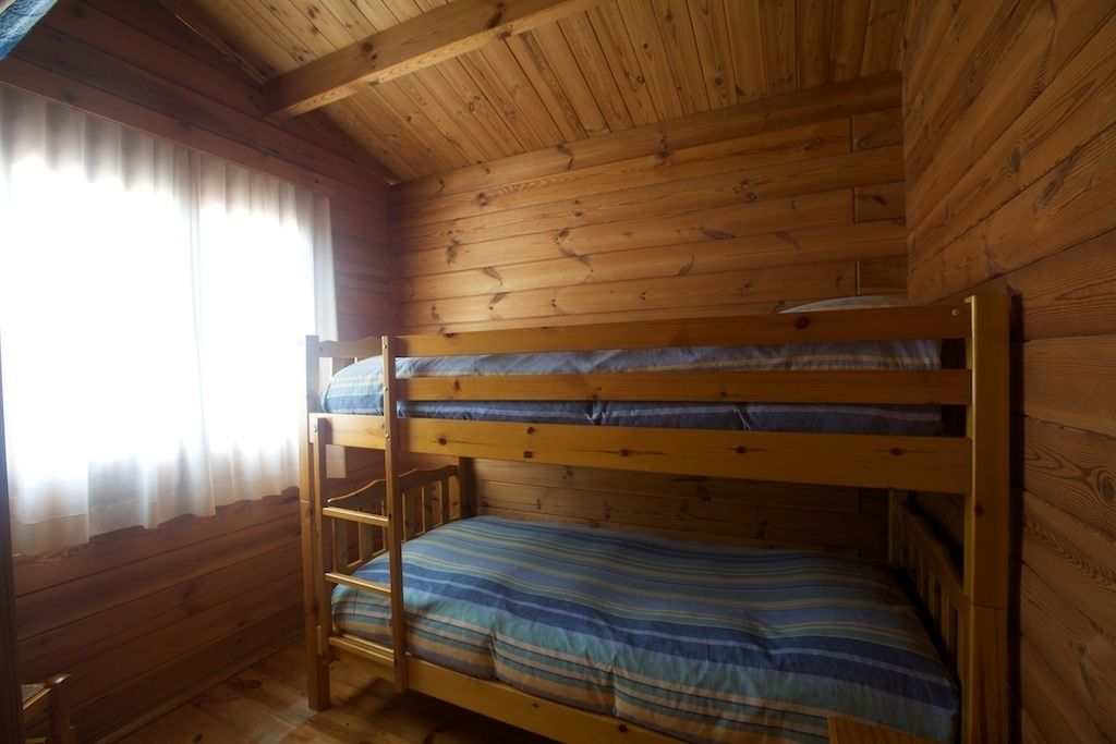 Una habitación de cabaña de madera con literas y una ventana con cortinas.